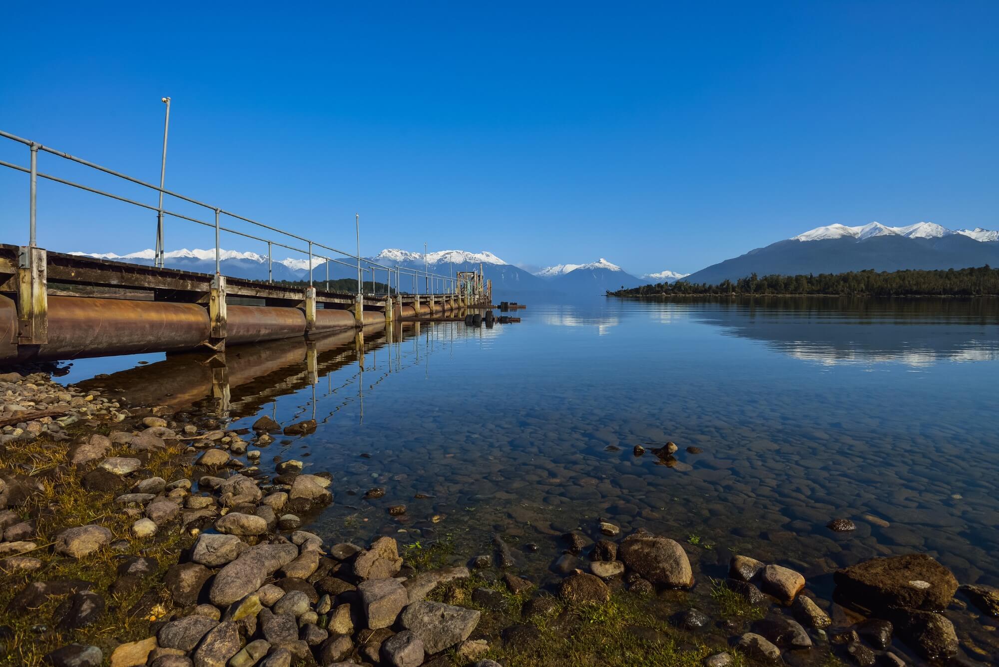 Lakeside,Jetty,With,Reflection,Of,Blue,Sky,And,Snow,Capped